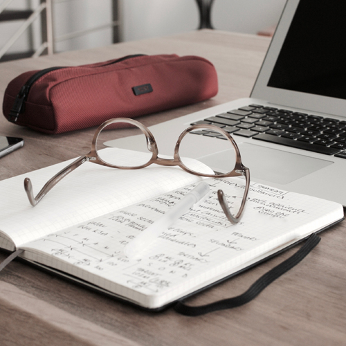 eyeglasses on a book with a desk and laptop